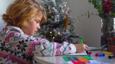 Noel Baba 'ya yeni yıl tatili için mektup yazan çocuk, rahat Noel süslemeleri ve ışıkları, renkli kalemler çizen kız, Noel Baba' ya hediyeler hazırlayan çocuk,