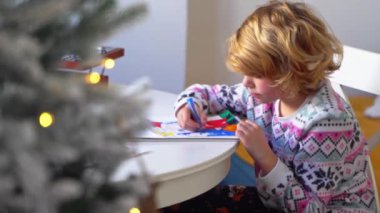 Noel Baba 'ya yeni yıl tatili için mektup yazan çocuk, rahat Noel süslemeleri ve ışıkları, renkli kalemler çizen kız, Noel Baba' ya hediyeler hazırlayan çocuk,