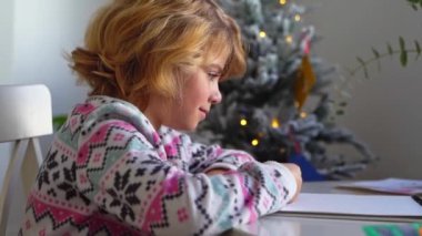 Noel Baba 'ya yeni yıl tatili için mektup yazan çocuk, rahat Noel süslemeleri ve ışıkları, renkli kalemler çizen kız, Noel Baba' ya hediyeler hazırlayan çocuk,