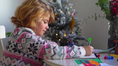 Noel Baba 'ya yeni yıl tatili için mektup yazan çocuk, rahat Noel süslemeleri ve ışıkları, renkli kalemler çizen kız, Noel Baba' ya hediyeler hazırlayan çocuk,