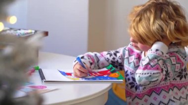 Noel Baba 'ya yeni yıl tatili için mektup yazan çocuk, rahat Noel süslemeleri ve ışıkları, renkli kalemler çizen kız, Noel Baba' ya hediyeler hazırlayan çocuk,