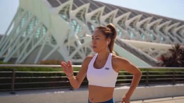 Spor kıyafetleriyle koşan Asyalı yetişkin kadın koşucu güneşli bir sabah kentsel yüksek teknoloji arka planında dantel takıyor. Koşu maratonu, dayanıklılık, kalp egzersizi sağlıklı yaşam tarzı.