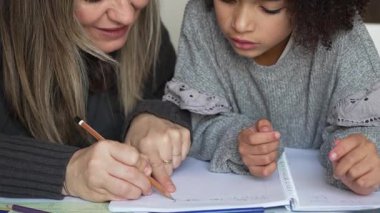 Kafkasyalı anne ve Afrikalı Amerikalı kız evde çalışıyor, rahat beyaz odada ödev yapıyor. Ebeveyn öğretmenliği, çocuk okulu kızı bilgi öğrenme, egzersiz kitabı yazma. Çocuklar için eğitim