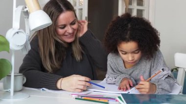 Kafkasyalı anne ve Afrikalı Amerikalı kız evde çalışıyor, rahat beyaz odada ödev yapıyor. Ebeveyn öğretmenliği, çocuk okulu kızı bilgi öğrenme, egzersiz kitabı yazma. Çocuklar için eğitim