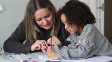 Kafkasyalı anne ve Afrikalı Amerikalı kız evde çalışıyor, rahat beyaz odada ödev yapıyor. Ebeveyn öğretmenliği, çocuk okulu kızı bilgi öğrenme, egzersiz kitabı yazma. Çocuklar için eğitim