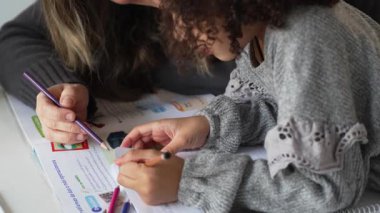 Kafkasyalı anne ve Afrikalı Amerikalı kız evde çalışıyor, rahat beyaz odada ödev yapıyor. Ebeveyn öğretmenliği, çocuk okulu kızı bilgi öğrenme, egzersiz kitabı yazma. Çocuklar için eğitim