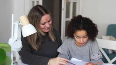 Kafkasyalı anne ve Afrikalı Amerikalı kız evde çalışıyor, rahat beyaz odada ödev yapıyor. Ebeveyn öğretmenliği, çocuk okulu kızı bilgi öğrenme, egzersiz kitabı yazma. Çocuklar için eğitim