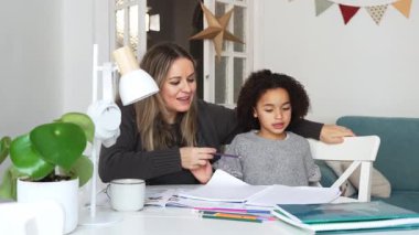 Kafkasyalı anne ve Afrikalı Amerikalı kız evde çalışıyor, rahat beyaz odada ödev yapıyor. Ebeveyn öğretmenliği, çocuk okulu kızı bilgi öğrenme, egzersiz kitabı yazma. Çocuklar için eğitim