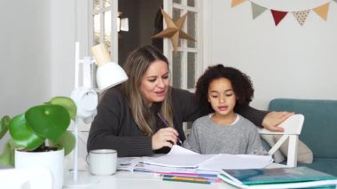 Kafkasyalı anne ve Afrikalı Amerikalı kız evde çalışıyor, rahat beyaz odada ödev yapıyor. Ebeveyn öğretmenliği, çocuk okulu kızı bilgi öğrenme, egzersiz kitabı yazma. Çocuklar için eğitim
