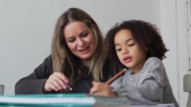 Kafkasyalı anne ve Afrikalı Amerikalı kız evde çalışıyor, rahat beyaz odada ödev yapıyor. Ebeveyn öğretmenliği, çocuk okulu kızı bilgi öğrenme, egzersiz kitabı yazma. Çocuklar için eğitim