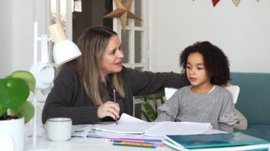 Kafkasyalı anne ve Afrikalı Amerikalı kız evde çalışıyor, rahat beyaz odada ödev yapıyor. Ebeveyn öğretmenliği, çocuk okulu kızı bilgi öğrenme, egzersiz kitabı yazma. Çocuklar için eğitim