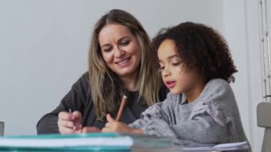 Kafkasyalı anne ve Afrikalı Amerikalı kız evde çalışıyor, rahat beyaz odada ödev yapıyor. Ebeveyn öğretmenliği, çocuk okulu kızı bilgi öğrenme, egzersiz kitabı yazma. Çocuklar için eğitim