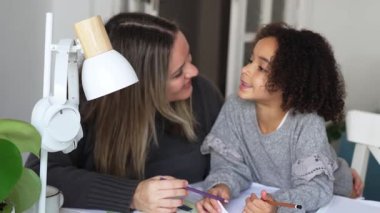 Kafkasyalı anne ve Afrikalı Amerikalı kız evde çalışıyor, rahat beyaz odada ödev yapıyor. Ebeveyn öğretmenliği, çocuk okulu kızı bilgi öğrenme, egzersiz kitabı yazma. Çocuklar için eğitim