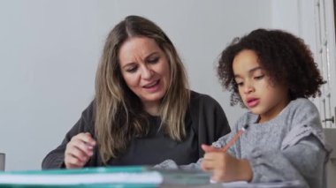 Kafkasyalı anne ve Afrikalı Amerikalı kız evde çalışıyor, rahat beyaz odada ödev yapıyor. Ebeveyn öğretmenliği, çocuk okulu kızı bilgi öğrenme, egzersiz kitabı yazma. Çocuklar için eğitim