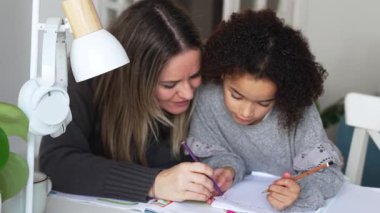 Kafkasyalı anne ve Afrikalı Amerikalı kız evde çalışıyor, rahat beyaz odada ödev yapıyor. Ebeveyn öğretmenliği, çocuk okulu kızı bilgi öğrenme, egzersiz kitabı yazma. Çocuklar için eğitim