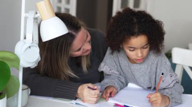 Kafkasyalı anne ve Afrikalı Amerikalı kız evde çalışıyor, rahat beyaz odada ödev yapıyor. Ebeveyn öğretmenliği, çocuk okulu kızı bilgi öğrenme, egzersiz kitabı yazma. Çocuklar için eğitim