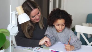 Kafkasyalı anne ve Afrikalı Amerikalı kız evde çalışıyor, rahat beyaz odada ödev yapıyor. Ebeveyn öğretmenliği, çocuk okulu kızı bilgi öğrenme, egzersiz kitabı yazma. Çocuklar için eğitim
