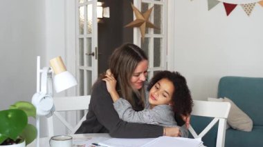 Kafkasyalı anne ve Afrikalı Amerikalı kız evde çalışıyor, rahat beyaz odada ödev yapıyor. Ebeveyn öğretmenliği, çocuk okulu kızı bilgi öğrenme, egzersiz kitabı yazma. Çocuklar için eğitim