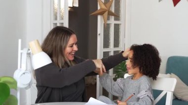 Kafkasyalı anne ve Afrikalı Amerikalı kız evde çalışıyor, rahat beyaz odada ödev yapıyor. Ebeveyn öğretmenliği, çocuk okulu kızı bilgi öğrenme, egzersiz kitabı yazma. Çocuklar için eğitim