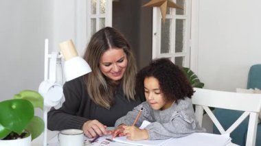 Kafkasyalı anne ve Afrikalı Amerikalı kız evde çalışıyor, rahat beyaz odada ödev yapıyor. Ebeveyn öğretmenliği, çocuk okulu kızı bilgi öğrenme, egzersiz kitabı yazma. Çocuklar için eğitim