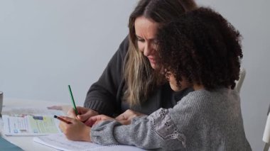 Kafkasyalı anne ve Afrikalı Amerikalı kız evde çalışıyor, rahat beyaz odada ödev yapıyor. Ebeveyn öğretmenliği, çocuk okulu kızı bilgi öğrenme, egzersiz kitabı yazma. Çocuklar için eğitim