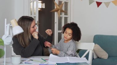 Kafkasyalı anne ve Afrikalı Amerikalı kız evde çalışıyor, rahat beyaz odada ödev yapıyor. Ebeveyn öğretmenliği, çocuk okulu kızı bilgi öğrenme, egzersiz kitabı yazma. Çocuklar için eğitim