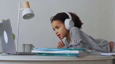 İlkokul Afro-Amerikan öğrenci kulaklıklı el yazısıyla dizüstü bilgisayar kullanıyor. Uzaktan öğrenme çevrimiçi eğitim. Liseli kız evde dijital tabletle çalışıyor.