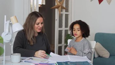 Kafkasyalı anne ve Afrikalı Amerikalı kız evde çalışıyor, rahat beyaz odada ödev yapıyor. Ebeveyn öğretmenliği, çocuk okulu kızı bilgi öğrenme, egzersiz kitabı yazma. Çocuklar için eğitim