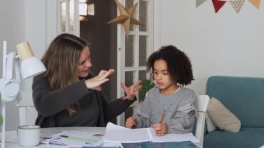 Kafkasyalı anne ve Afrikalı Amerikalı kız evde çalışıyor, rahat beyaz odada ödev yapıyor. Ebeveyn öğretmenliği, çocuk okulu kızı bilgi öğrenme, egzersiz kitabı yazma. Çocuklar için eğitim