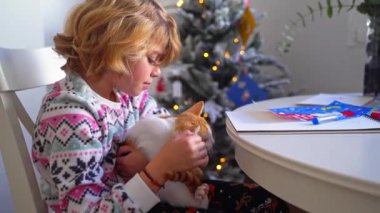 Noel Baba 'ya yılbaşı mektubu yazan çocuk kızıl kedisi, rahat Noel süsü ve ışıklarıyla, renkli kalemler çizen kız aileye hediyeler hazırlıyor, oğlum.