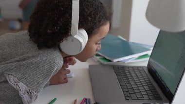 İlkokul Afro-Amerikan öğrenci kulaklıklı el yazısıyla dizüstü bilgisayar kullanıyor. Uzaktan öğrenme çevrimiçi eğitim. Liseli kız evde dijital tabletle çalışıyor.