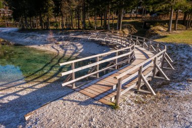Tahta köprü sola doğru kıvrılıyor ve gölgelerde don var. Slovenya, Kranjska Gora 'da Jasna Gölü yakınında.