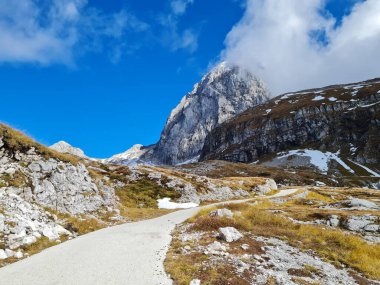 Mangart tepesi bulutların içinde bir dağ yolunun üzerinden çayırların arasından geçiyor.