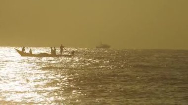 Güneşin doğuşunda balıkçıyla birlikte teknenin silueti Horizon Sunrise sahilinde güzel bir gün doğumu. Okyanus ve altın güneş doğuyor, parlak altın arka plan. Güneşin batışında dramatik bulutlu gökyüzünün olduğu güzel manzara. turuncu 
