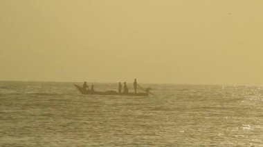Güneşin doğuşunda balıkçıyla birlikte teknenin silueti Horizon Sunrise sahilinde güzel bir gün doğumu. Okyanus ve altın güneş doğuyor, parlak altın arka plan. Güneşin batışında dramatik bulutlu gökyüzünün olduğu güzel manzara. turuncu 