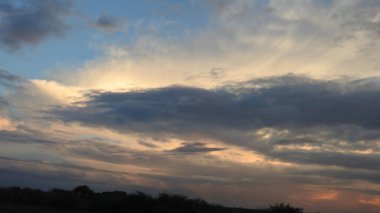 Günbatımı fotoğrafı, gün batımında bulutlu gökyüzü. Bulutlar ve mavi gökyüzü. Tasarım ve arkaplan için panoramik fotoğraf. Çöl batımı, günbatımında suya yansıyan ağaç ve binalarla ufuk çizgisi manzarası. Altın Günbatımı Bulutları. Renkli turuncu gün batımı. 