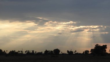 Günbatımı fotoğrafı, gün batımında bulutlu gökyüzü. Bulutlar ve mavi gökyüzü. Tasarım ve arkaplan için panoramik fotoğraf. Çöl batımı, günbatımında suya yansıyan ağaç ve binalarla ufuk çizgisi manzarası. Altın Günbatımı Bulutları. Renkli turuncu gün batımı. 