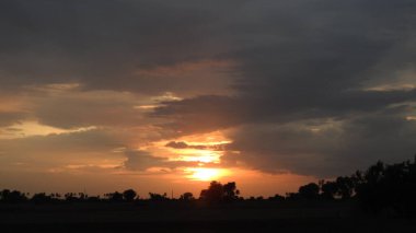 Günbatımı fotoğrafı, gün batımında bulutlu gökyüzü. Bulutlar ve mavi gökyüzü. Tasarım ve arkaplan için panoramik fotoğraf. Çöl batımı, günbatımında suya yansıyan ağaç ve binalarla ufuk çizgisi manzarası. Altın Günbatımı Bulutları. Renkli turuncu gün batımı. 
