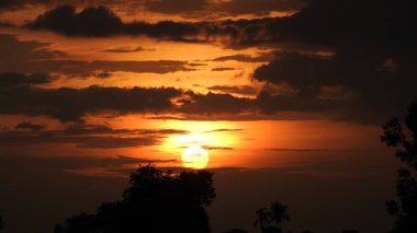 Günbatımı fotoğrafı, gün batımında bulutlu gökyüzü. Bulutlar ve mavi gökyüzü. Tasarım ve arkaplan için panoramik fotoğraf. Çöl batımı, günbatımında suya yansıyan ağaç ve binalarla ufuk çizgisi manzarası. Altın Günbatımı Bulutları. Renkli turuncu gün batımı. 