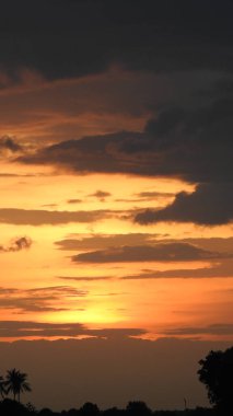 Günbatımı fotoğrafı, gün batımında bulutlu gökyüzü. Bulutlar ve mavi gökyüzü. Tasarım ve arkaplan için panoramik fotoğraf. Çöl batımı, günbatımında suya yansıyan ağaç ve binalarla ufuk çizgisi manzarası. Altın Günbatımı Bulutları. Renkli turuncu gün batımı. 