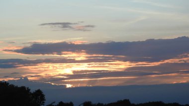 Siluet günbatımı. Düz ufuk ve ağaçlarla mükemmel renkli günbatımı. Palmiye ağaçları ve sudaki insanların siluetleri. Güzel sahil manzarasında gün batımında birçok insan gün batımından önce denize oynamaya gelir. Sahilde günbatımının silueti.