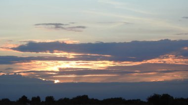 Siluet günbatımı. Düz ufuk ve ağaçlarla mükemmel renkli günbatımı. Palmiye ağaçları ve sudaki insanların siluetleri. Güzel sahil manzarasında gün batımında birçok insan gün batımından önce denize oynamaya gelir. Sahilde günbatımının silueti.