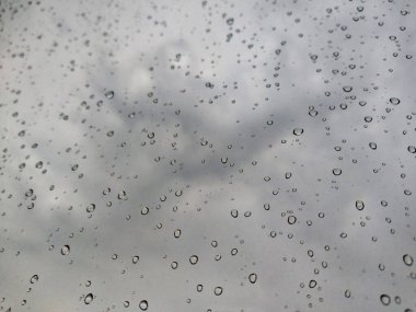 Fırtına sırasında pencere camında büyük yağmur damlaları vardı. Bulutların, yeşil ağaçların ve binaların manzarası. Fırtınalı bir günde yağmur damlalarının şehir manzarası pencereye düşer. Pencereye yağmur damlası. Cama yağmur damlaları. Otomotiv üzerine yağmur damlaları 