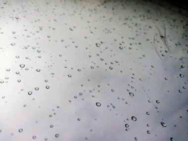 Fırtına sırasında pencere camında büyük yağmur damlaları vardı. Bulutların, yeşil ağaçların ve binaların manzarası. Fırtınalı bir günde yağmur damlalarının şehir manzarası pencereye düşer. Pencereye yağmur damlası. Cama yağmur damlaları. Otomotiv üzerine yağmur damlaları 