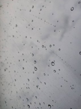 Fırtına sırasında pencere camında büyük yağmur damlaları vardı. Bulutların, yeşil ağaçların ve binaların manzarası. Fırtınalı bir günde yağmur damlalarının şehir manzarası pencereye düşer. Pencereye yağmur damlası. Cama yağmur damlaları. Otomotiv üzerine yağmur damlaları 