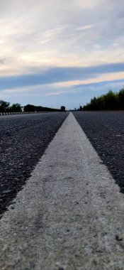 Terk edilmiş asfalt yol ve şafak vakti dağ manzarası, hava yolu asfalt yolu ve güzel gökyüzü manzarası. Güneşli bir yaz gününde ufka giden boş uzun dağ yolu. Gün batımında. Hızlı hareket bulanıklığı etkisi. Asfalt yol ve göl gökyüzü