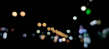 Soyut renkli bulanık ışıklar siyah arkaplanda hareket halinde. Ampullerin ışığına odaklanıyor. Soyut sahte arka plan, bulanık şehir ışıkları. Parlayan pırıltılı parlak arkaplanlı bulanık bir Noel arkaplanı. Soyut arkaplan