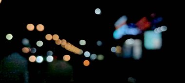 Soyut renkli bulanık ışıklar siyah arkaplanda hareket halinde. Ampullerin ışığına odaklanıyor. Soyut sahte arka plan, bulanık şehir ışıkları. Parlayan pırıltılı parlak arkaplanlı bulanık bir Noel arkaplanı. Soyut arkaplan