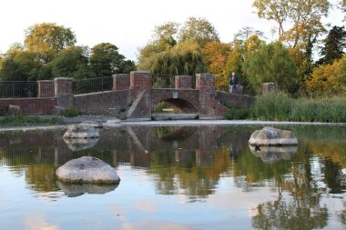 Autumn park bridge with rocks on a lake. Fall photography with trees and water reflection