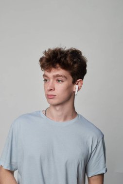 Gri arka planı olan bir fotoğraf stüdyosunda kulaklık takan genç bir adamın yan görüntüsü.